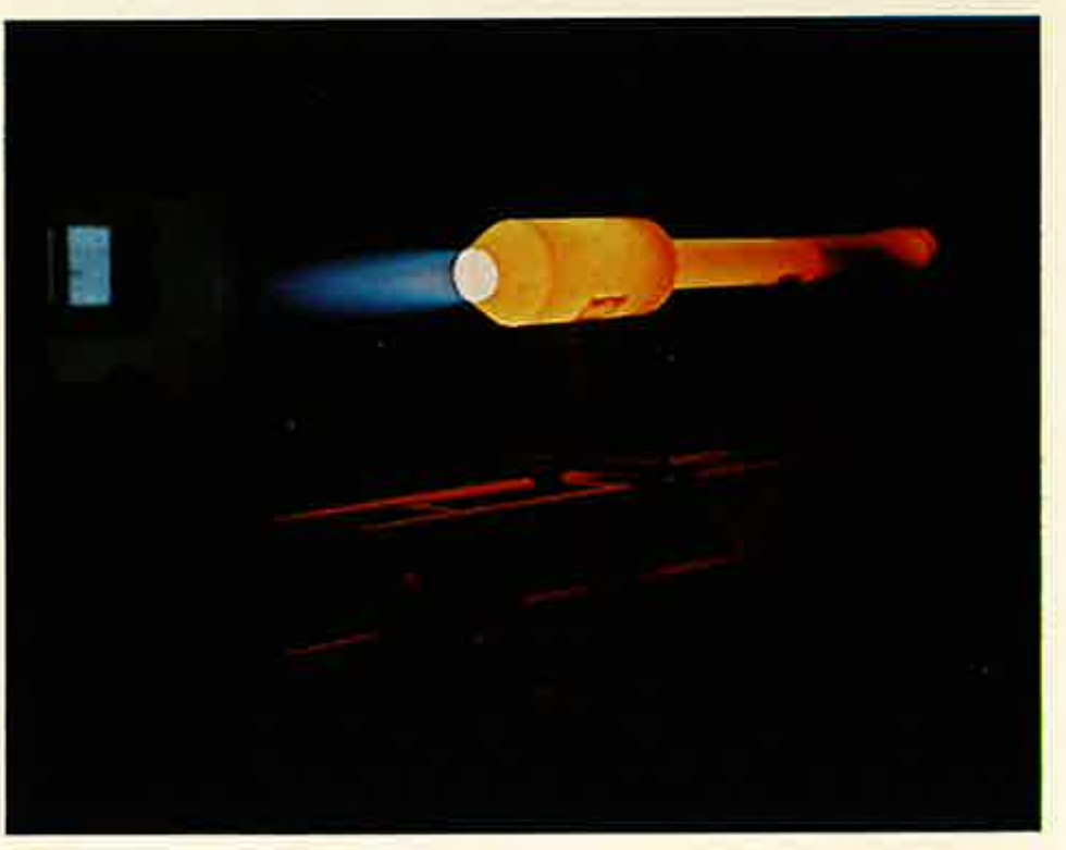 Colour photograph taken in darkness: a cylindrical engine glowing orange along its length, with a blue flame at the valve end and a faint red exhaust plume; the test rig frame glows dull red below.